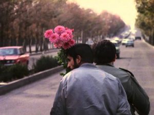 Sabzian en una motocicleta con otro hombre, cargando unas flores